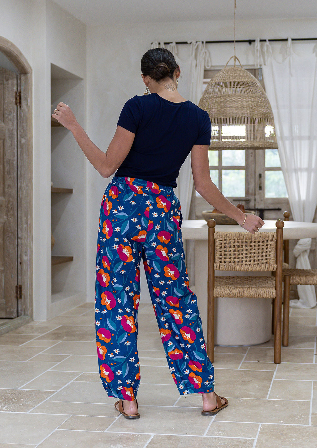 Model stands backwards wearing a 100% cotton printed wide leg cotton pants featuring pleated ankles and pockets