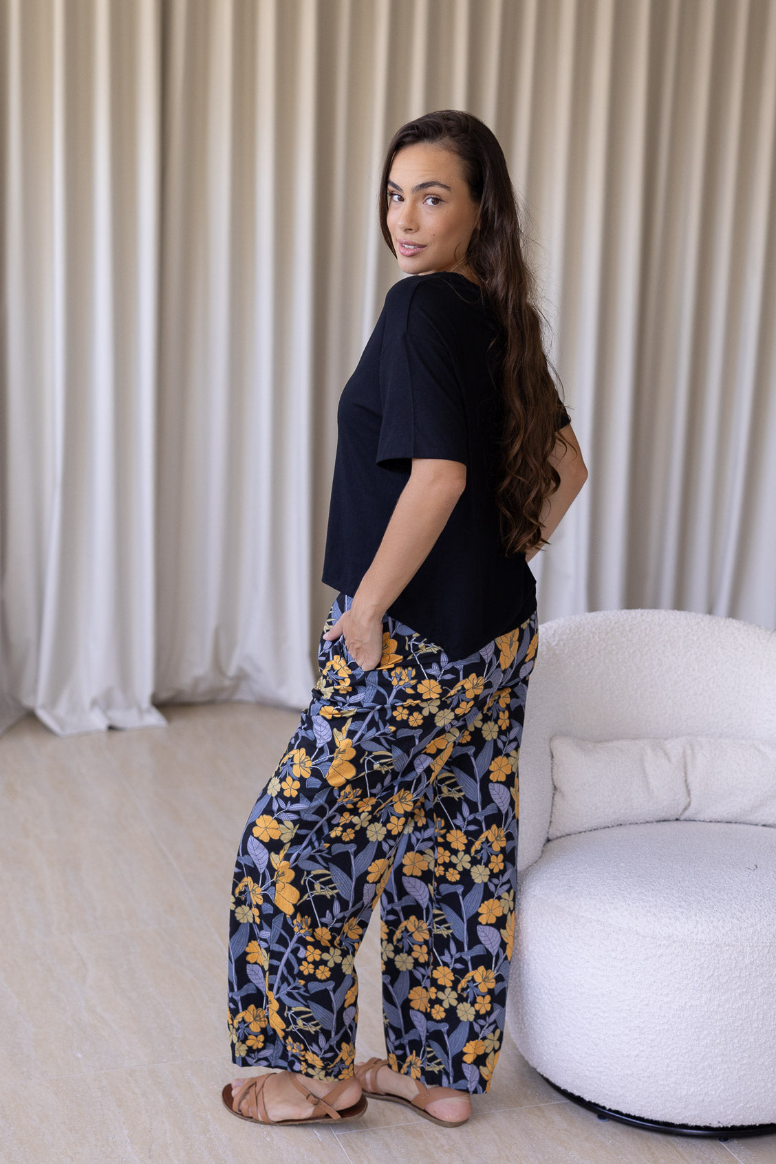 Woman wearing a black basic top and floral cotton wide-leg pants with elastic waist and pleated ankles in black based yellow and grey floral print