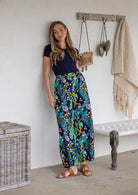 Woman wearing a 100% cotton wide leg pants in navy based multicolour floral print with pleats at the ankle.