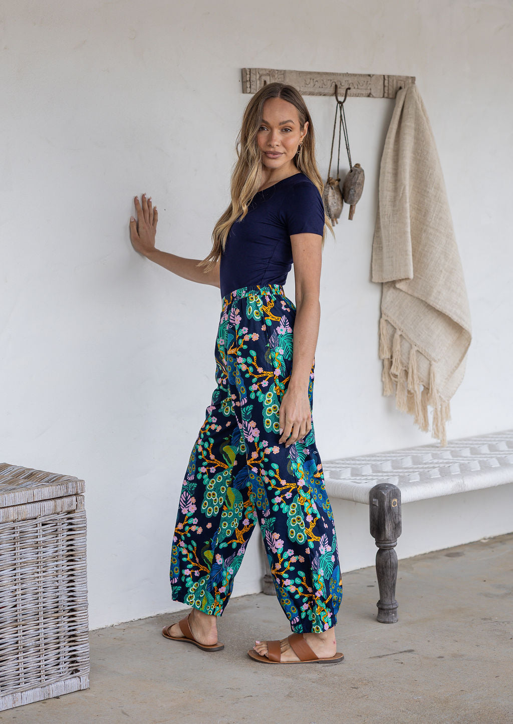Woman stands sideways wearing a 100% cotton wide leg pants in navy based multicolour floral print with pockets