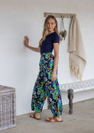 Woman stands sideways wearing a 100% cotton wide leg pants in navy based multicolour floral print with pockets