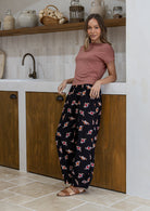 Woman wearing a pink top and dark floral print wide leg cotton pants with pleated ankles, elastic waist and pockets