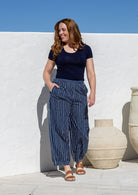 Woman wearing a 100% cotton wide leg pants in navy based white striped print with pockets and pleats at the ankle.