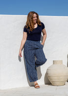 A woman wearing a navy blue basic top and navy blue and white vertically striped wide-leg pants, posing outdoors. 