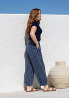 Woman stands sideways wearing a 100% cotton wide leg pants in navy based striped print with one hand in pocket 