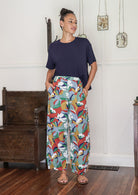 Woman wearing a basic top and colourful floral cotton pants with hand in pockets standing in a decorative indoor setting. 
