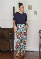Woman wearing a navy top and colorful patterned pants in a room with wooden furniture.