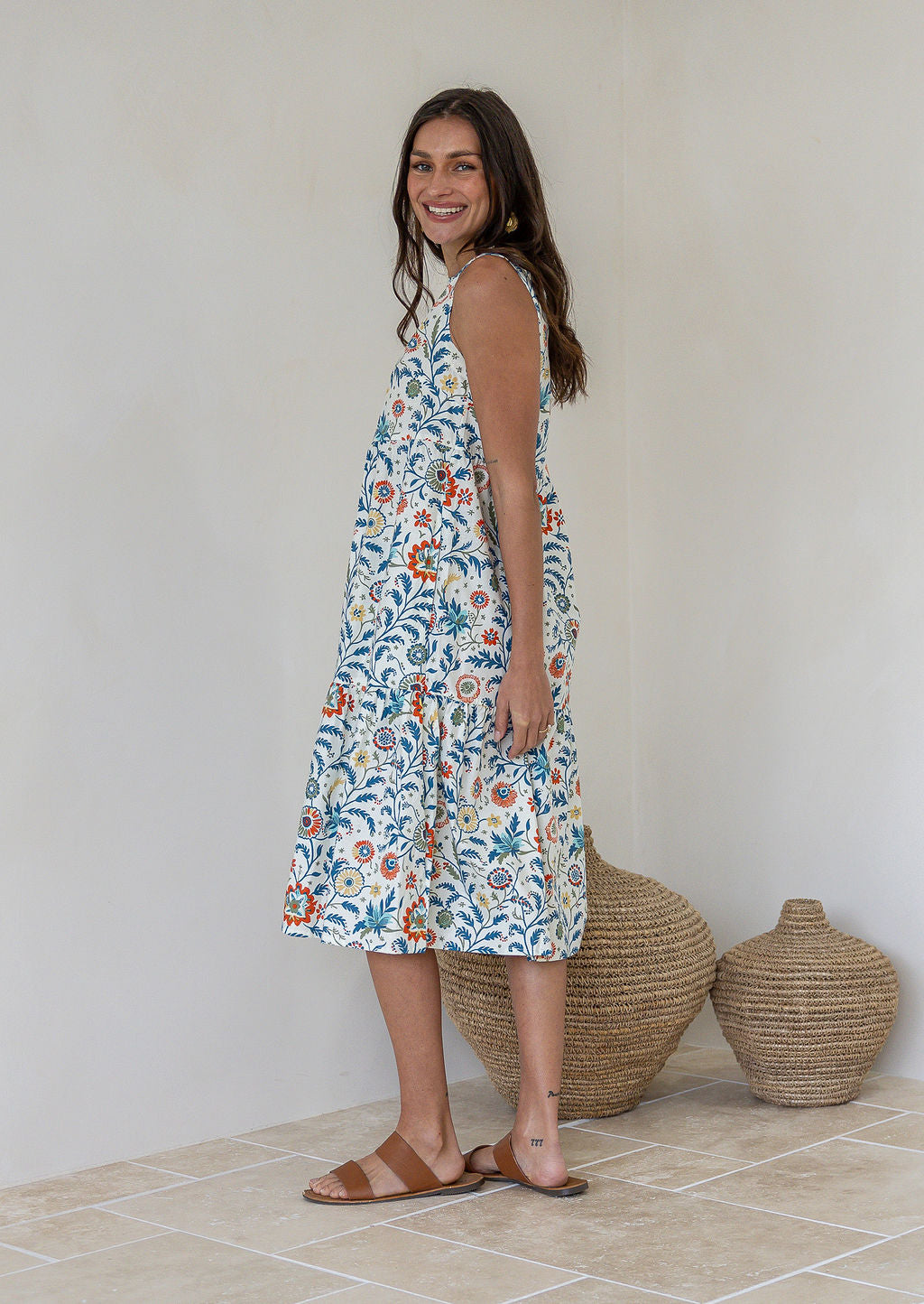 Woman stands sideways wearing a sleeveless cotton midi dress with two tiered design and high round neckline