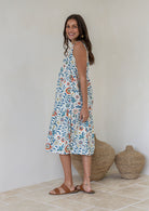 Woman stands sideways wearing a sleeveless cotton midi dress with two tiered design and high round neckline