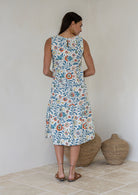 Woman stands backwards wearing a sleeveless cotton midi dress with two tiered design and high round neckline