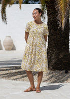 Woman poses in a cream based cotton floral short sleeve dress with round neckline