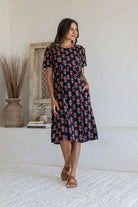 Woman poses in a black based cotton floral short sleeve dress with round neckline