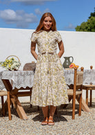 Woman wears retro style cotton button through midi length dress with high round neckline, short sleeves and a removable waist tie.
