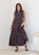 Woman wearing a 100% cotton black floral tiered maxi dress with sleeveless design and notch neckline. 