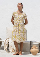 Woman wearing a 100% cotton Etta Dress in Primrose, yellow floral print, V-neck short-sleeve midi dress. 