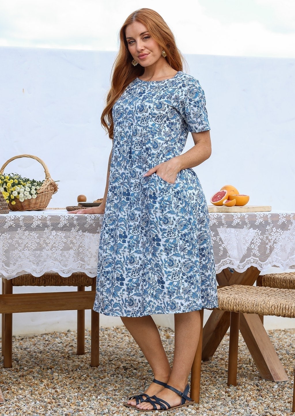 Woman poses in a white based cotton blue floral short sleeve dress with round neckline