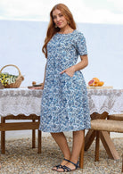 Woman poses in a white based cotton blue floral short sleeve dress with round neckline