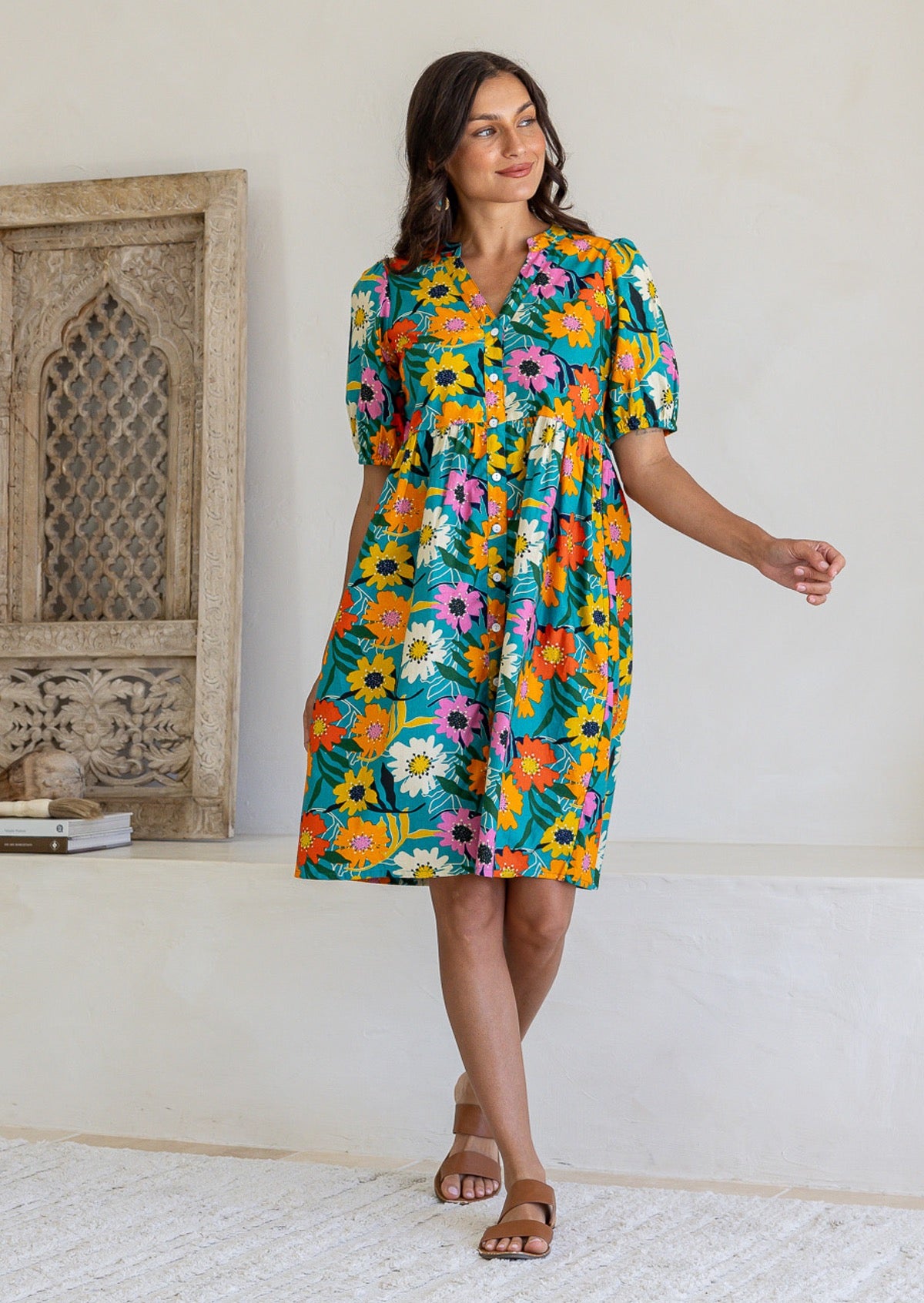 Woman wearing a 100% cotton teal floral Riley Dress with orange, pink, yellow wildflower print, puff sleeves. 