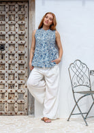Woman posing wearing a cotton sleeveless top in white based blue floral print with small decorative pleats in the front.