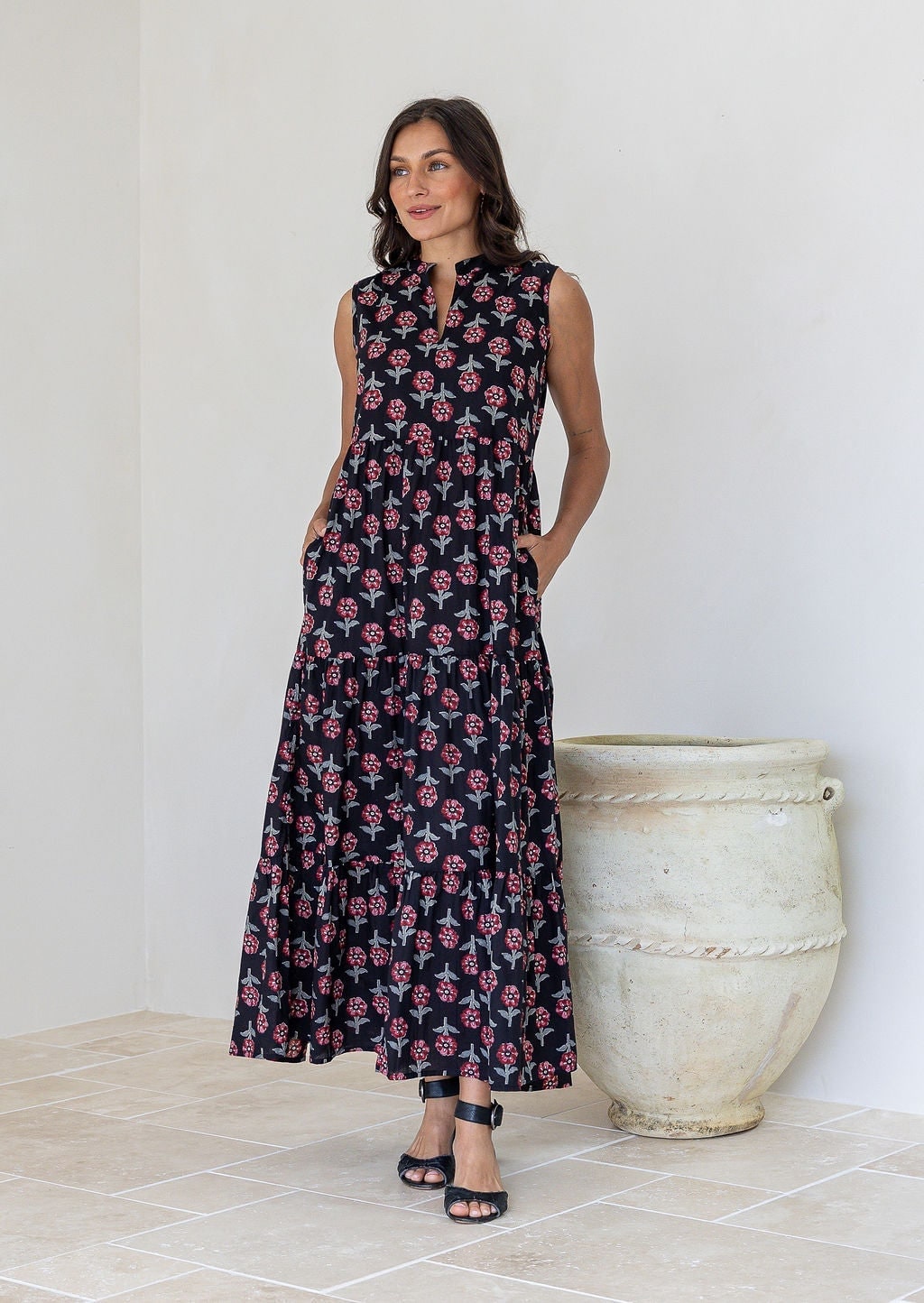 Woman wears sleeveless tiered maxi dress in black floral print with hand in pockets