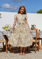 Woman wears 100% cotton button through midi length dress with short sleeves and pockets in floral print on a cream base.