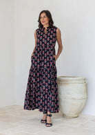 Woman wears sleeveless tiered maxi dress in black floral print with hand in pockets