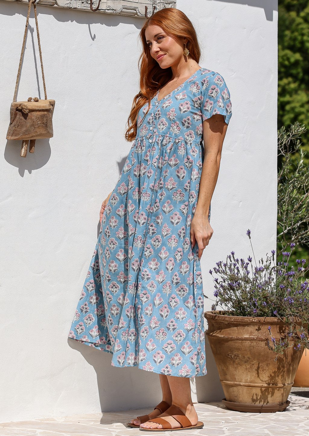 Woman stands sideways wearing a 100% cotton dress with short sleeves, pockets, and a drawstring tie at the back.