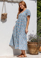 Woman stands sideways wearing a 100% cotton dress with short sleeves, pockets, and a drawstring tie at the back.