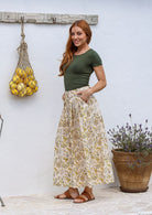 Woman wearing a 100% cotton Cora Skirt Primrose, cream floral maxi skirt with pockets, worn with olive top. 