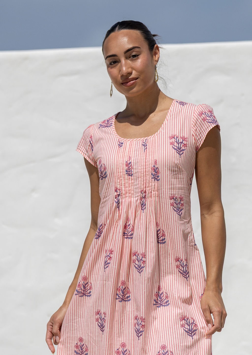 Woman wearing a 100% cotton Pink striped dress with floral print, cap sleeves and pintuck bodice. 