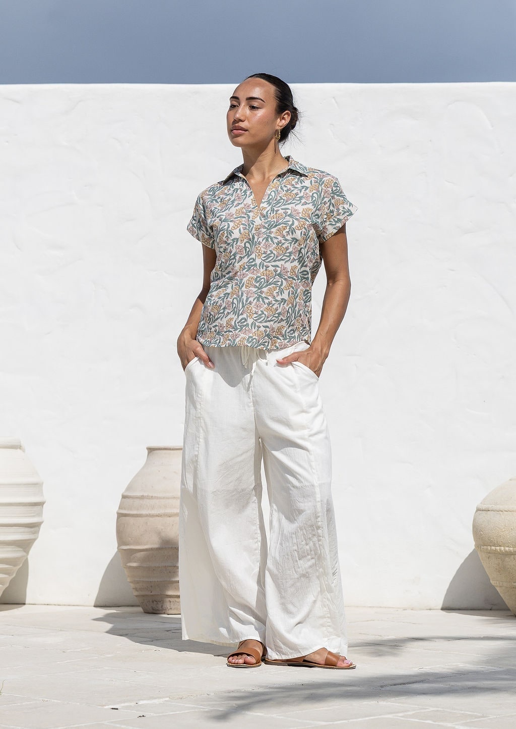 Woman wearing a floral 100% cotton top with short folded cuff sleeves paired with plain white pants