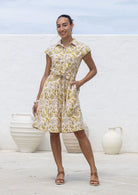 Woman wears fit and flare style shirt dress, 100% cotton with collar, cap sleeves, and removable waist tie in cream based floral print.