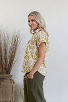Woman standing sideways wearing a floral cotton top with short folded cuff sleeves, collar and V neckline