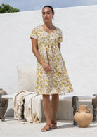 Woman wearing a cotton Etta Dress Primrose yellow floral print knee-length dress with V-neck. 