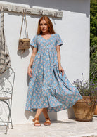 A woman wearing a powder blue cotton midi dress with short sleeves, a V-neckline, and is button-through. 