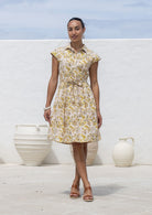 Model stands wearing a 100% cotton knee length shirt style retro floral dress in cream based floral print.