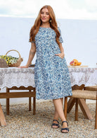 Woman poses in a white based cotton blue floral short sleeve dress with round neckline