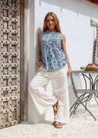 Model wears blue floral sleeveless pin tuck top with white wide-leg pants