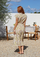 Model stands backwards wearing a mid length, shirt style floral print cotton dress with cream based floral print