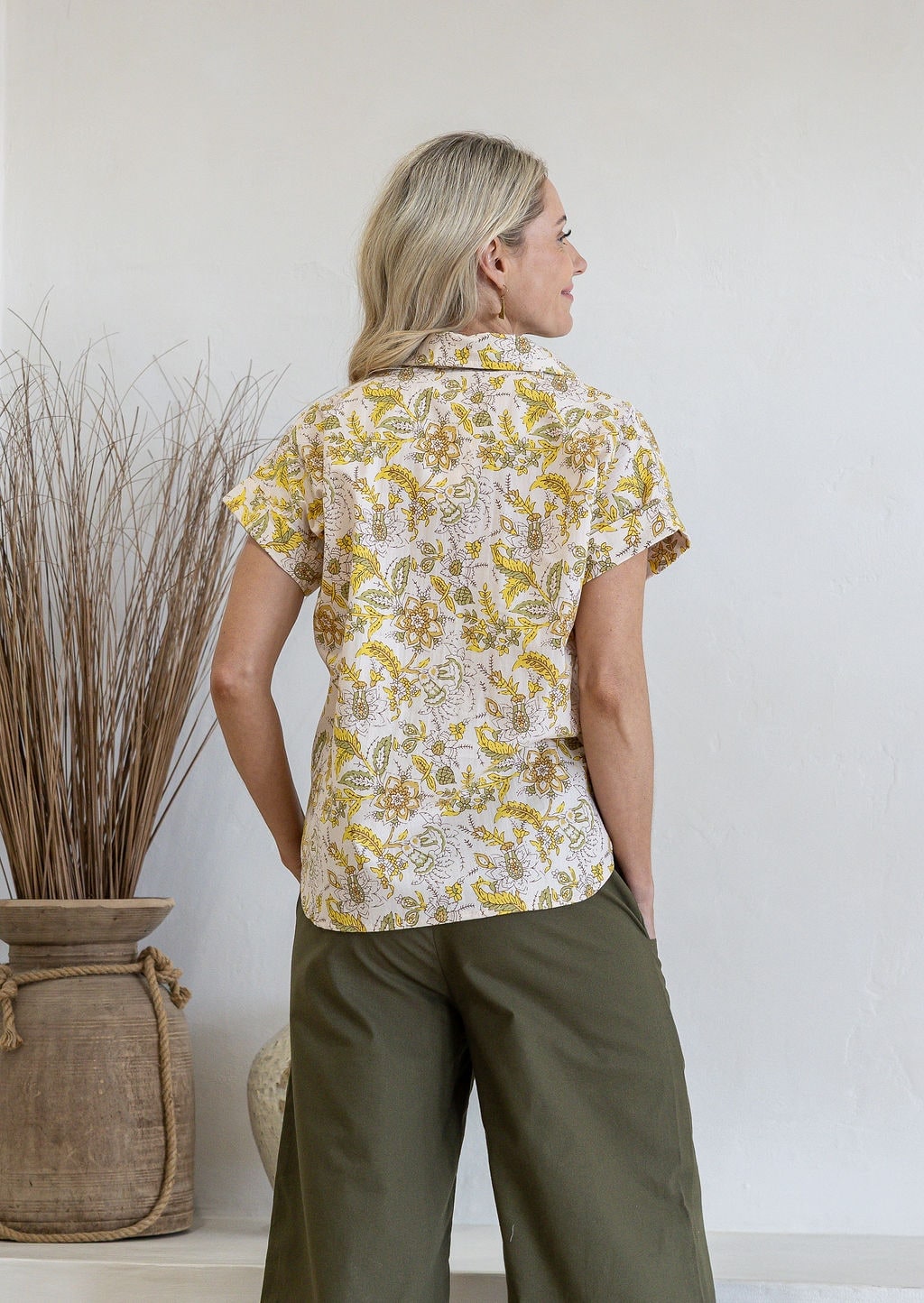 Woman standing backwards wearing a floral cotton top with short folded cuff sleeves, collar and V neckline