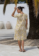 Woman stands backwards wearing a 100% cotton dress in cream based floral print with short sleeves. 
