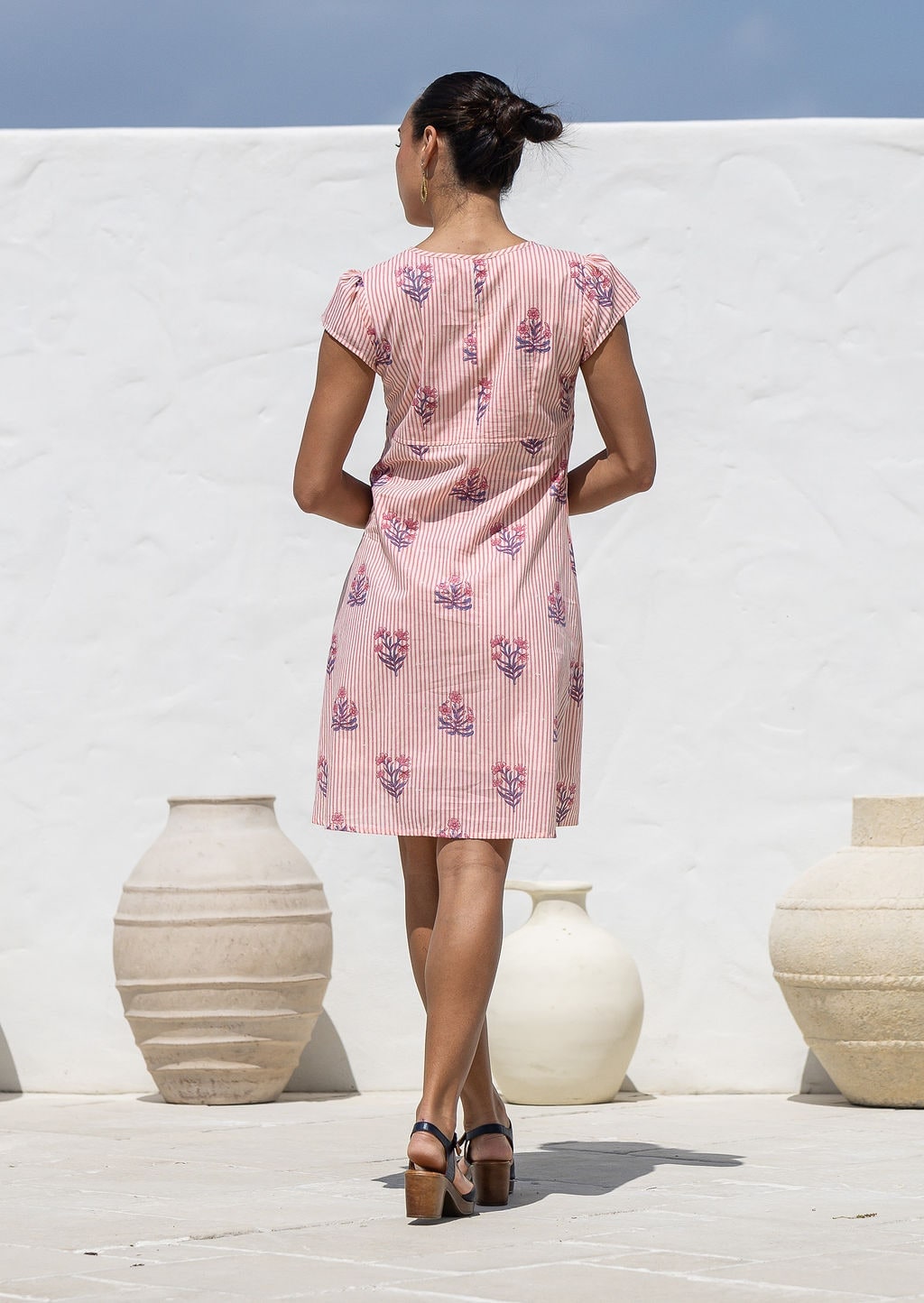 Woman stands backwards wearing a Pink floral-print short-sleeve floral cotton dress. 