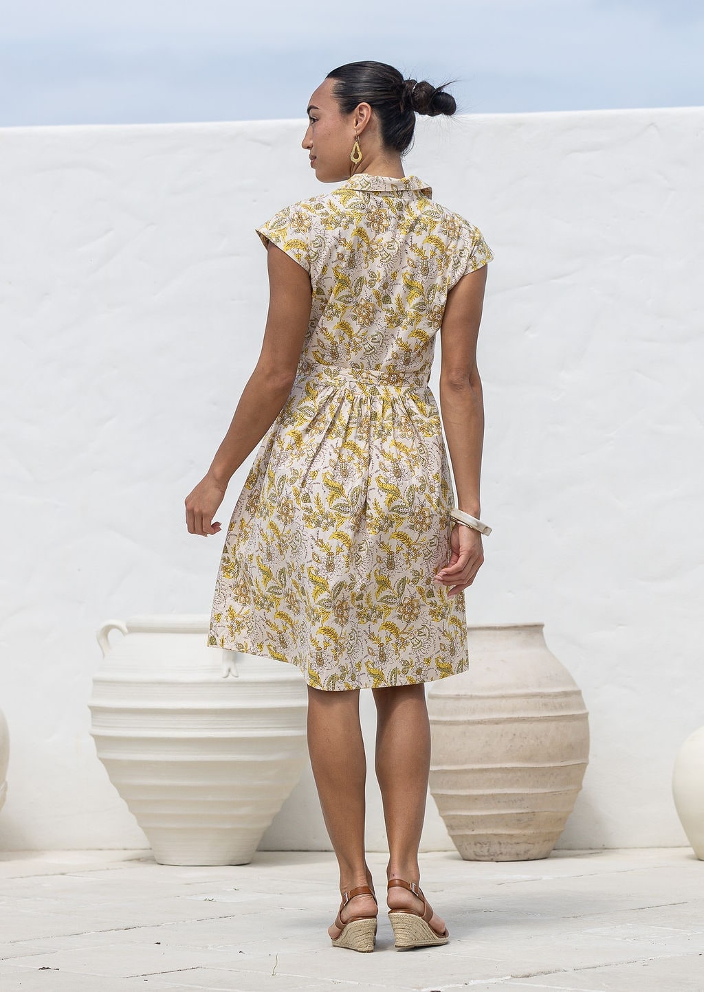 Woman stands backwards wears fit and flare style shirt dress, 100% cotton with collar, cap sleeves, and removable waist tie. 