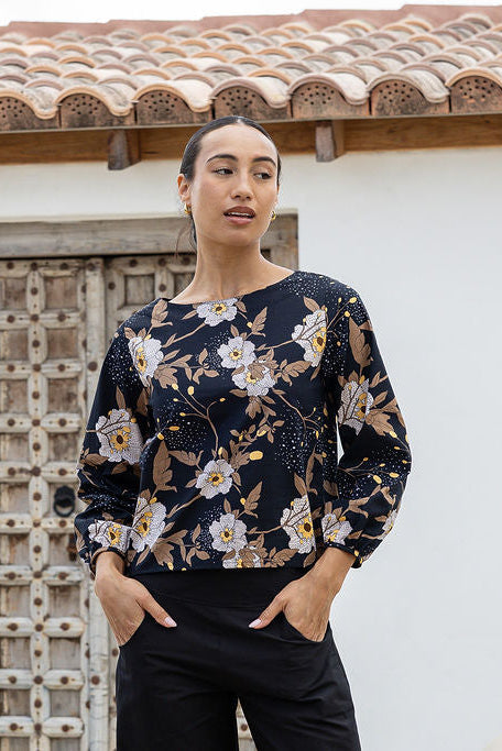 Woman wearing a floral top standing in front of a rustic wooden door.