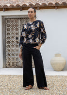 Woman wearing a black based floral, loose-fitting, long sleeved cotton top with a wide round neckline in camellia print.