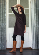 Woman wearing a dark brown dress, brown boots, and a beige hat indoors.