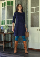 Woman wearing navy blue corduroy A-line dress with 3/4 sleeves over leggings and boots
