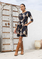 Woman wearing a 100% cotton floral dress with brown boots standing in front of a rustic wooden door.