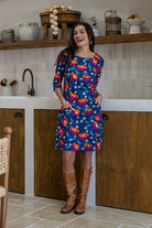 A woman wearing a 100% cotton knee-length dress in navy based floral print with 3/4 sleeves and both hand in pockets