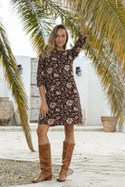 woman wearing a 100% cotton dress in black based floral print with round neckline and hand in pockets